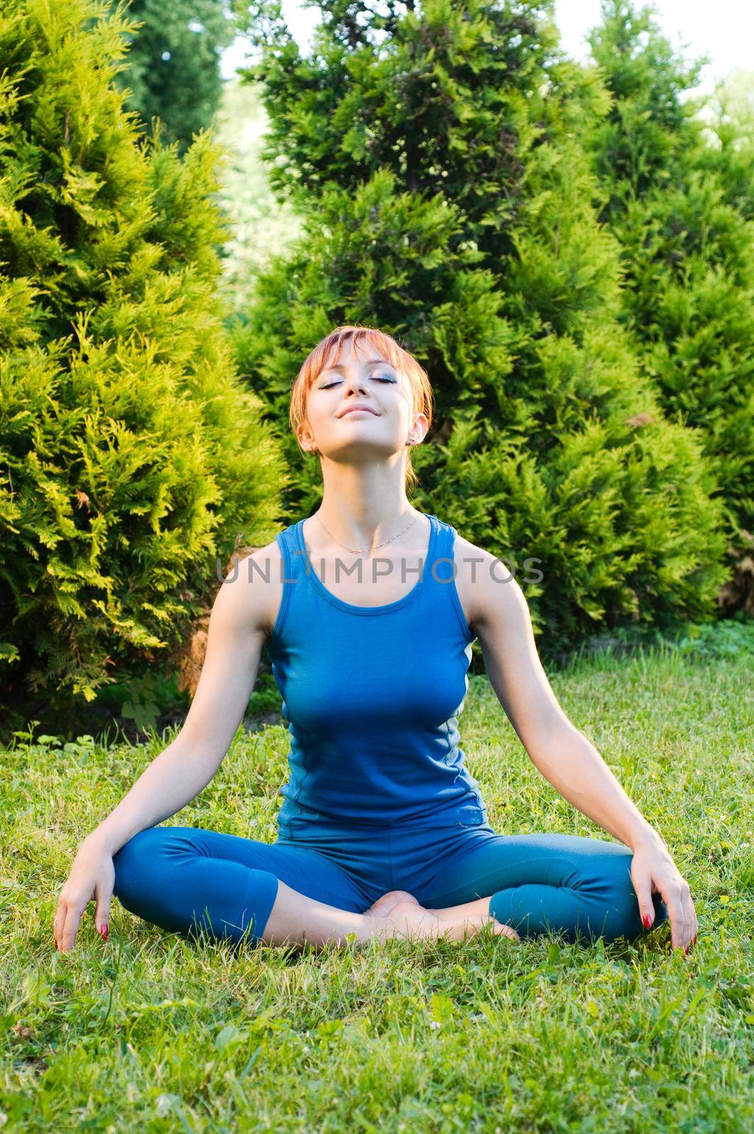 Beautiful red woman doing fitness or yoga exercises outdoors in a green park