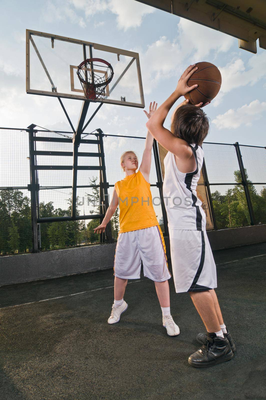 Two teenagers playing basketball at the street playground