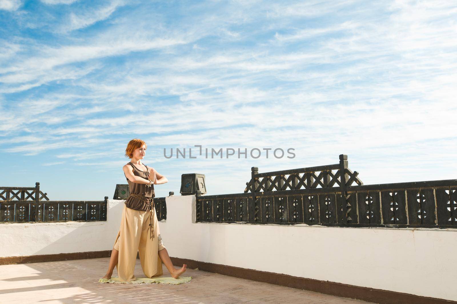 Beautiful young dancer performing yoga-dance outdoors with blue sky and clouds in the background