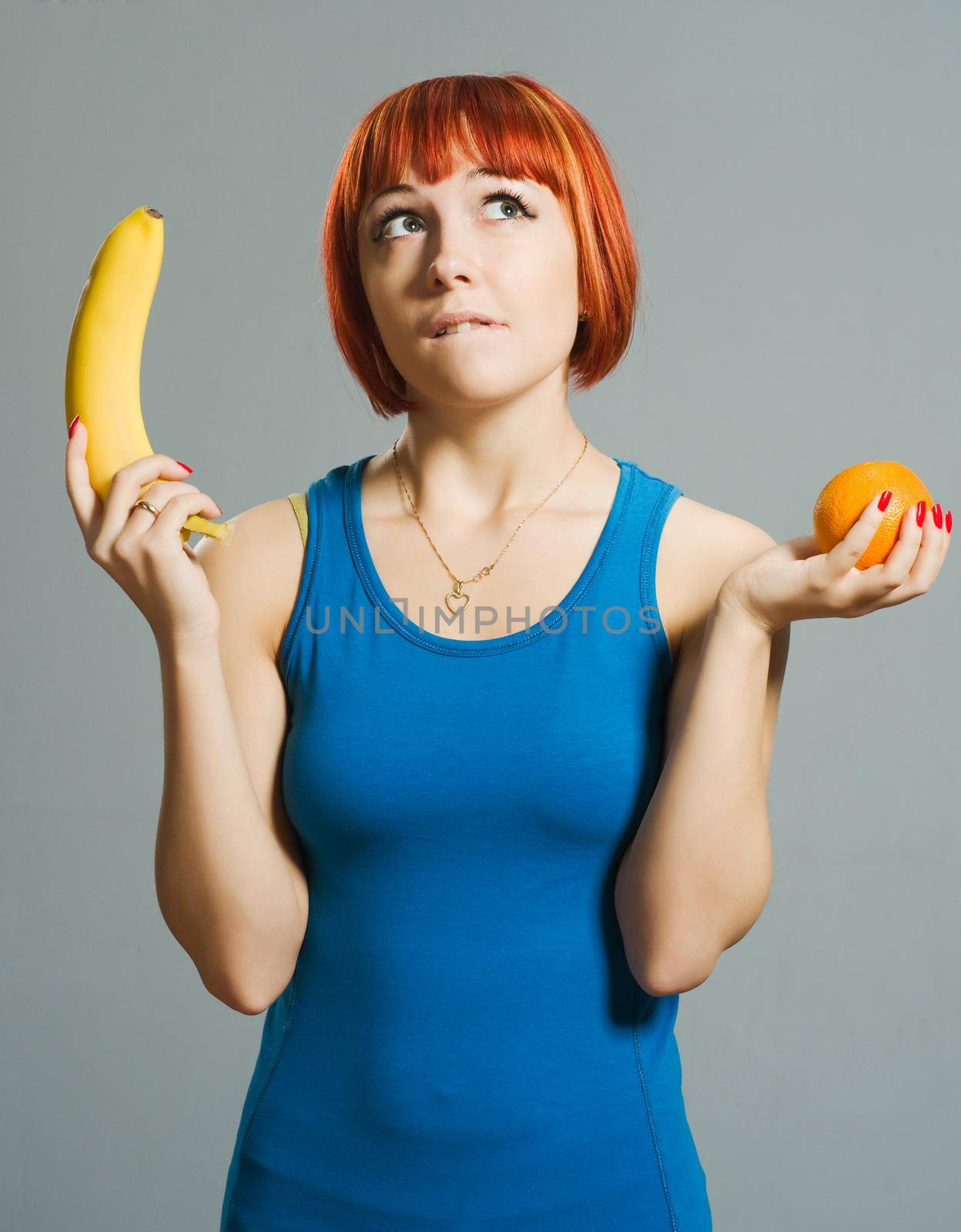 Red-haired girl with banana and orange in her hands
