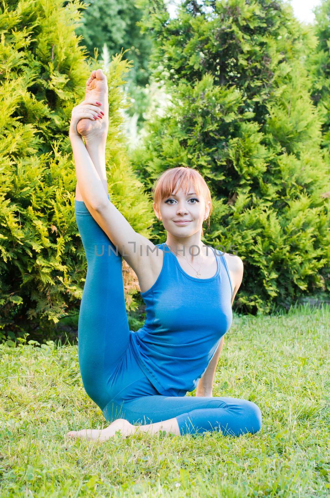 Beautiful red woman doing fitness or yoga exercises outdoors in a green park