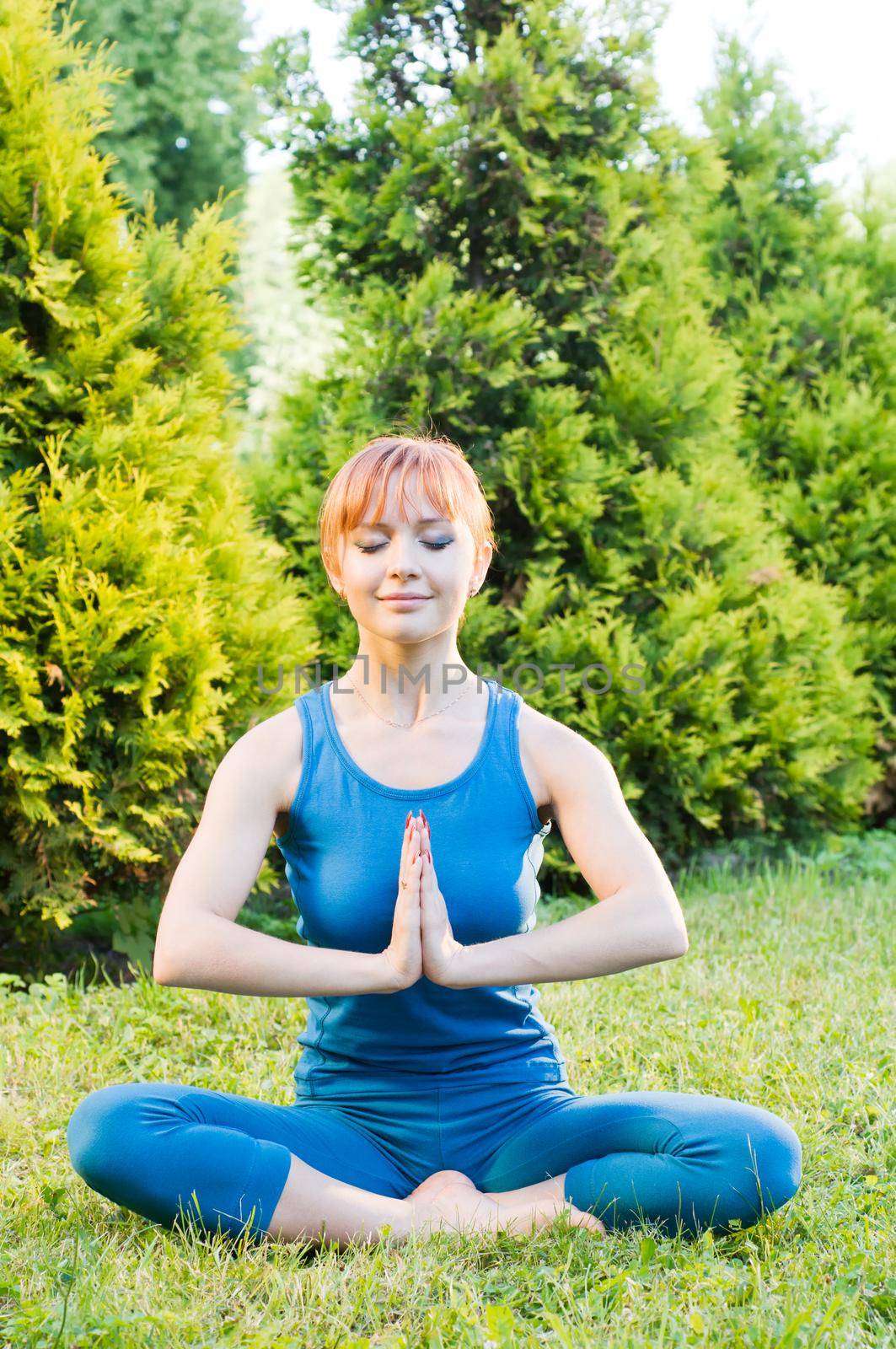 Beautiful red woman doing fitness or yoga exercises outdoors in a green park