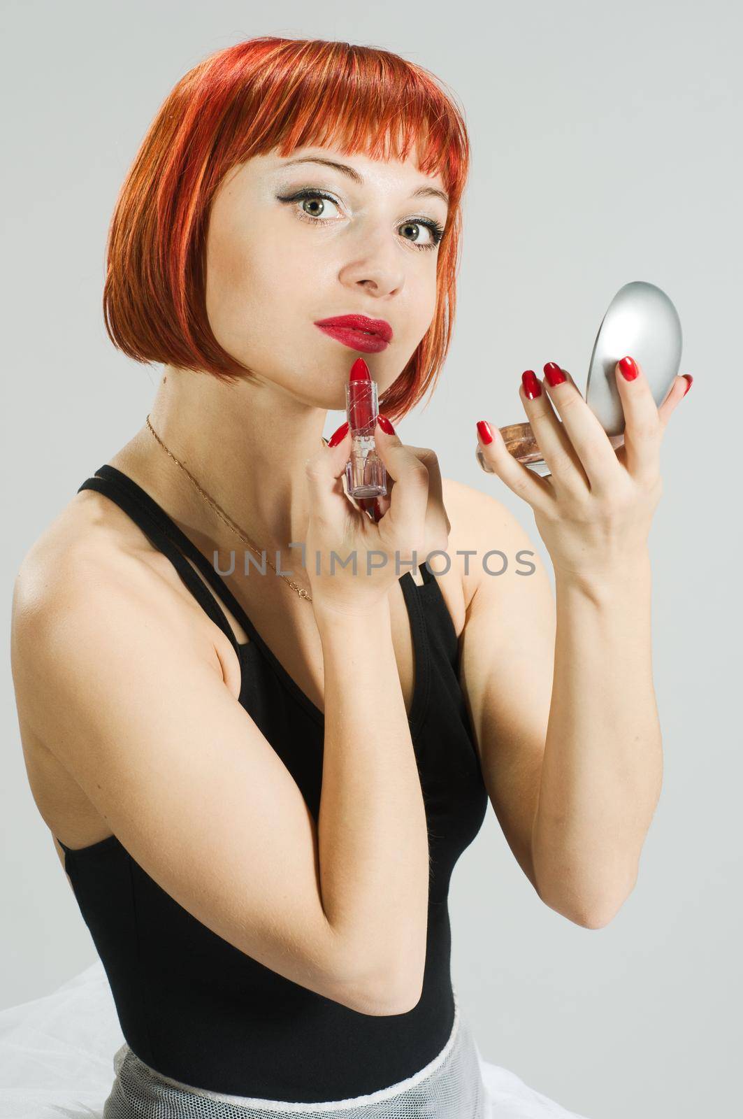 Beautiful red girl performing makeup using lipstick and mirror