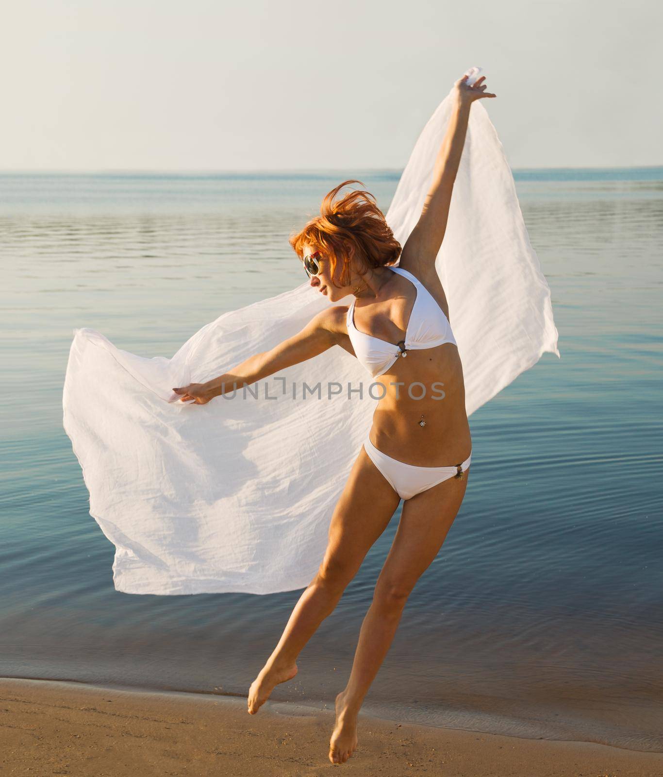 Beautiful redhair girl jumping with veil at the beach