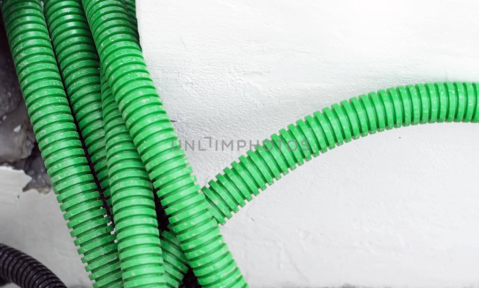 Corrugated tubular conduits ready to be filled with electrical cables on a construction site. White wall in the background. Construction material for securing electrical cables