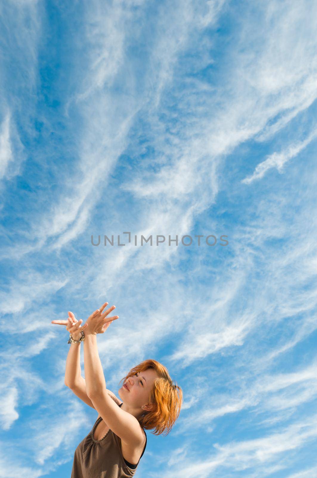 Beautiful young dancer performing yoga-dance outdoors with blue sky and clouds in the background