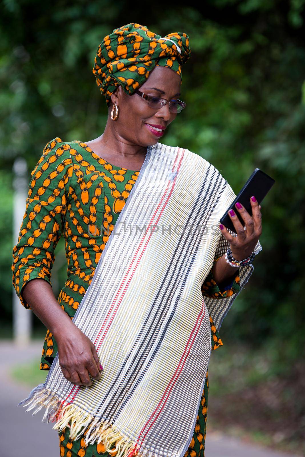 young african woman standing in loincloth and glasses looking at mobile phone while smiling.