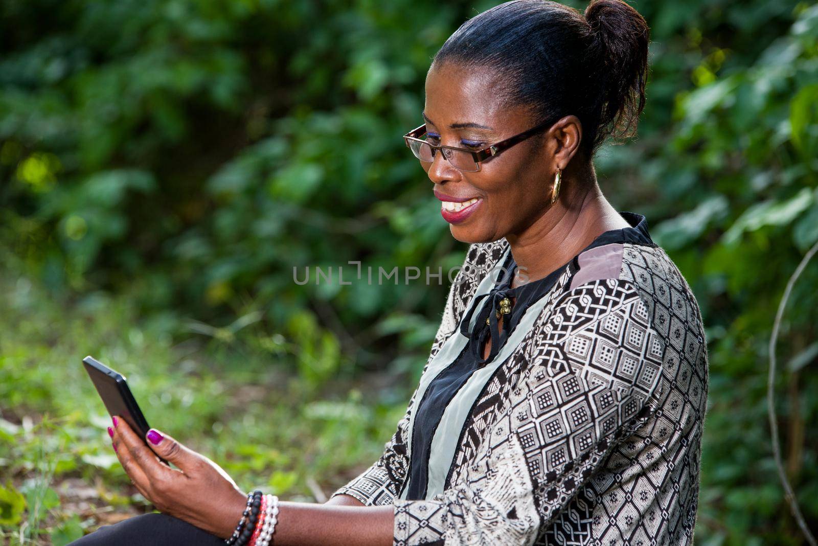 Beautiful woman resting in the forest speaks by mobile phone sitting at the park in casual clothes. Close up of big greenery in the park and holding the smart phone. technology and communication concept