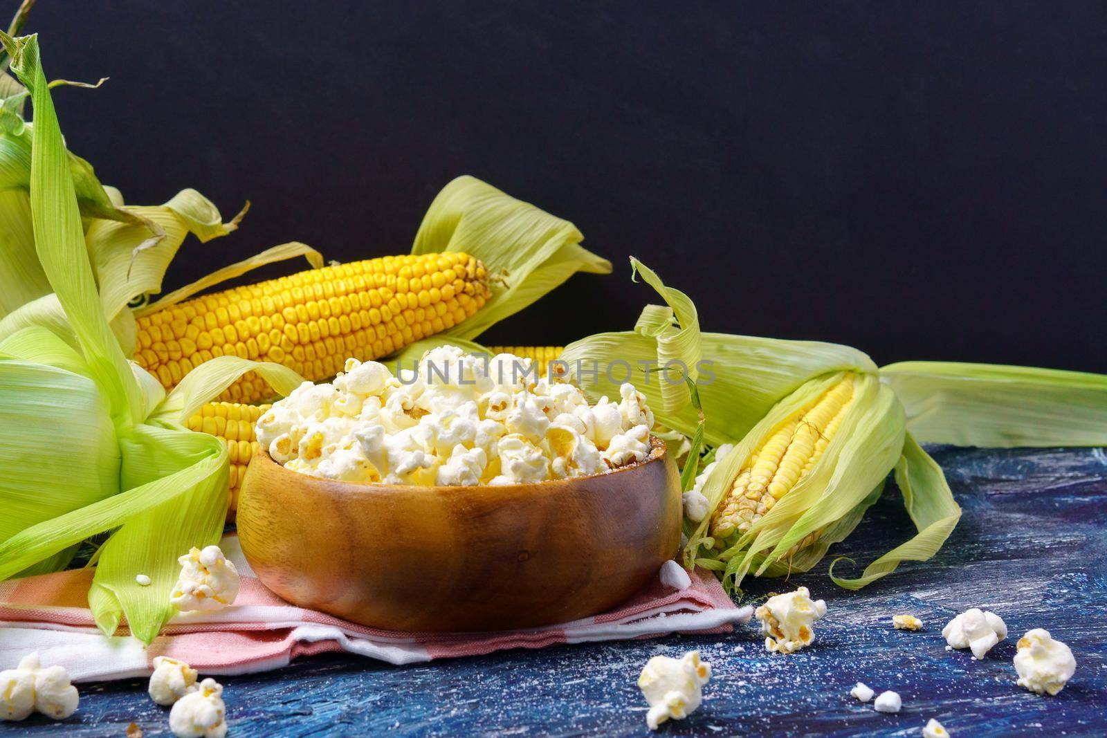 Tasty popcorn in a bowl on the table. Ears of fresh corn on a dark background. Copyspace by darksoul72