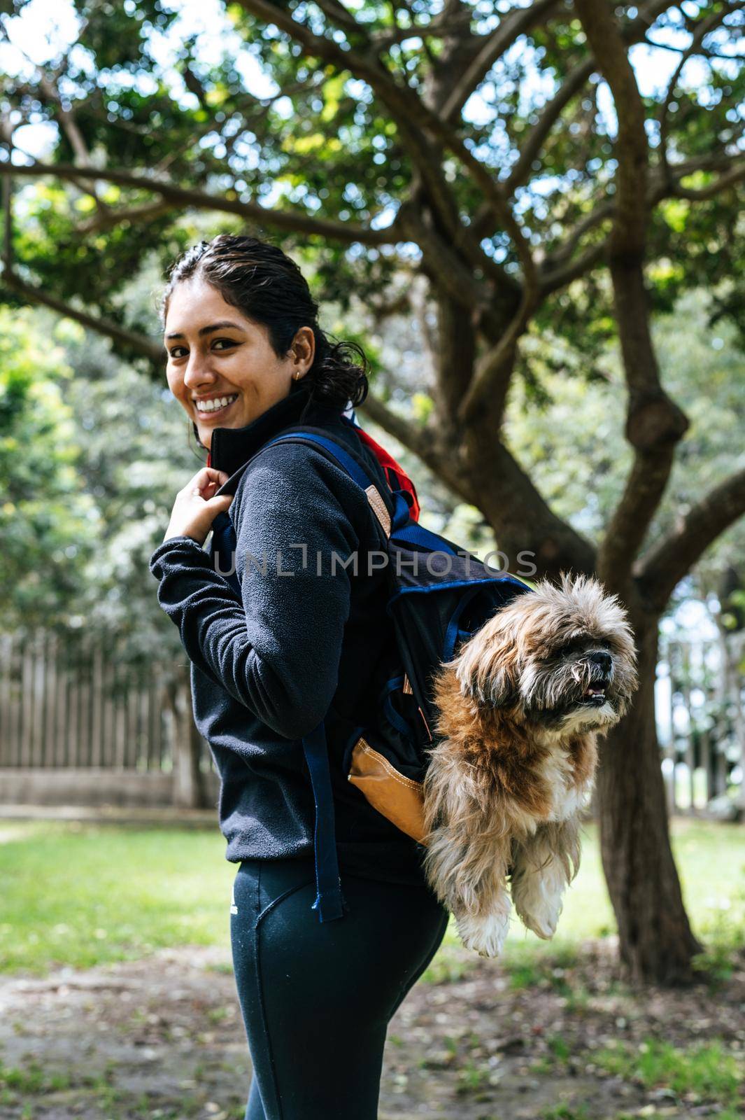 A charming young woman walks in nature, with a backpack on her shoulder, from which her dog peeks out. Concept relationship and love towards animals