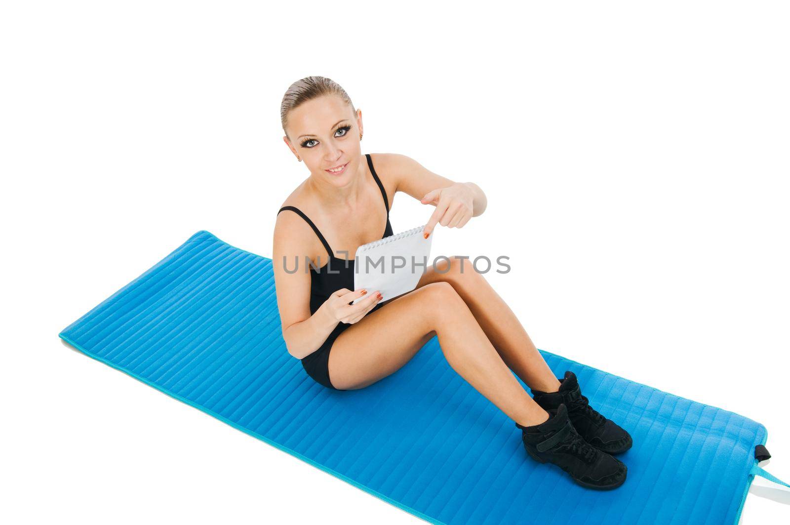 Beautiful fit red girl practicing pilates or callanetics with written plan on a blue yoga mat