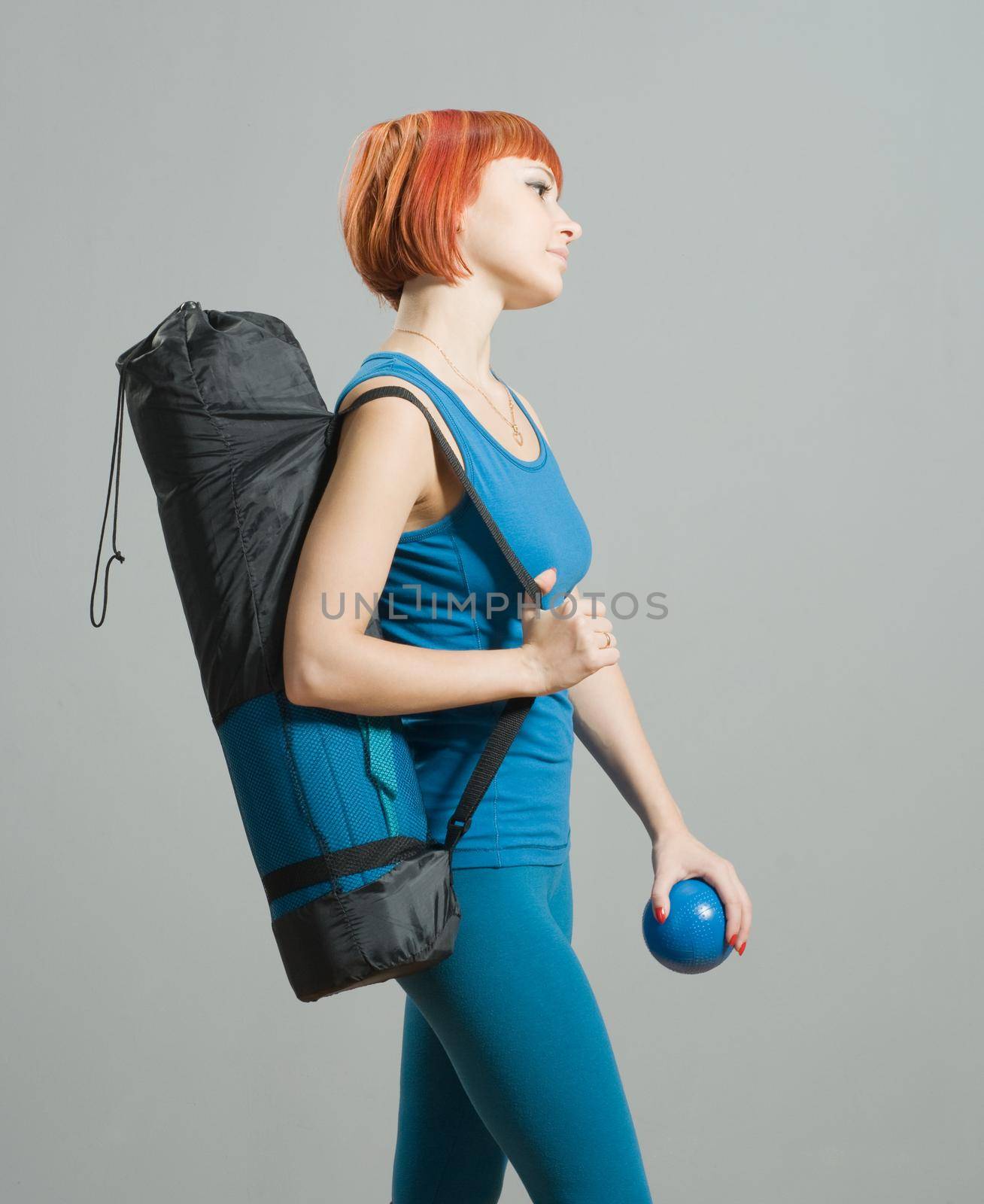 Red-haired fitness girl with yoga mat at the gym