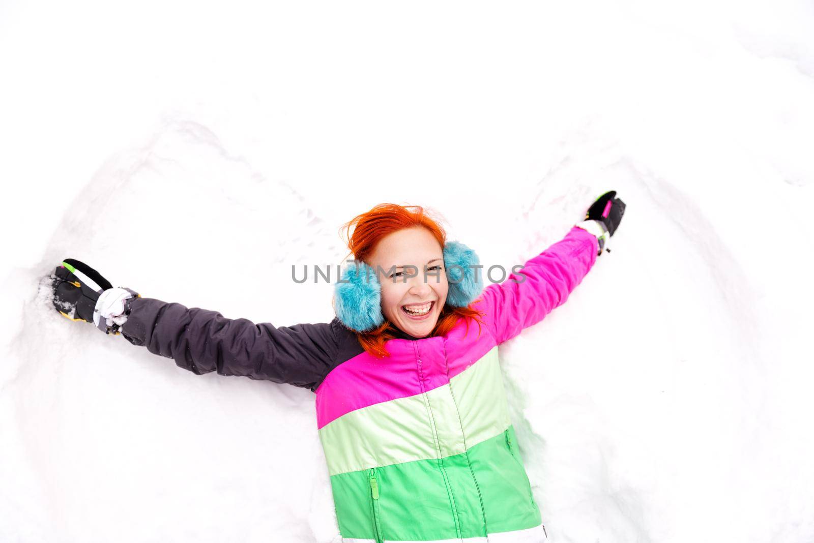 Cheerful girl wearing earphones playing snow angel