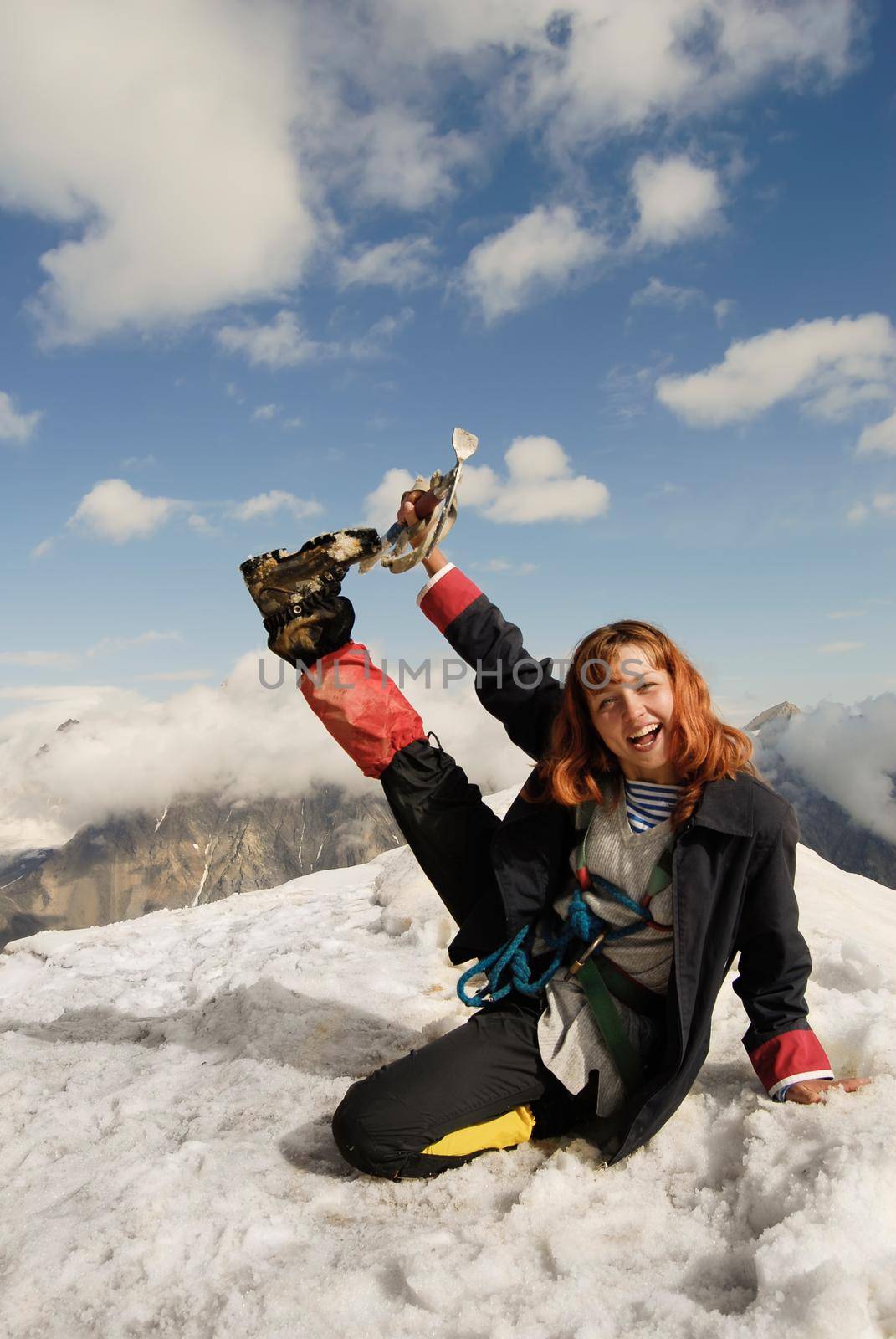 Red haired girl cheering at the top of a high mountain with ice-axe in her hand