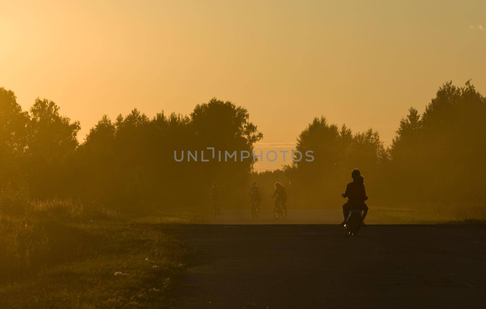 Golden sunset. Two boys riding a small bike and three girls on a bicycles