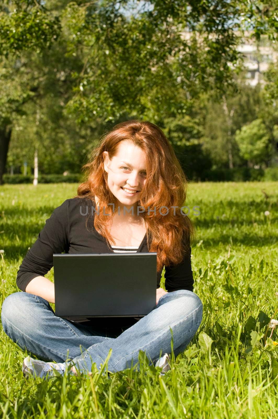 Beautiful red haired girl with laptop on a green grass