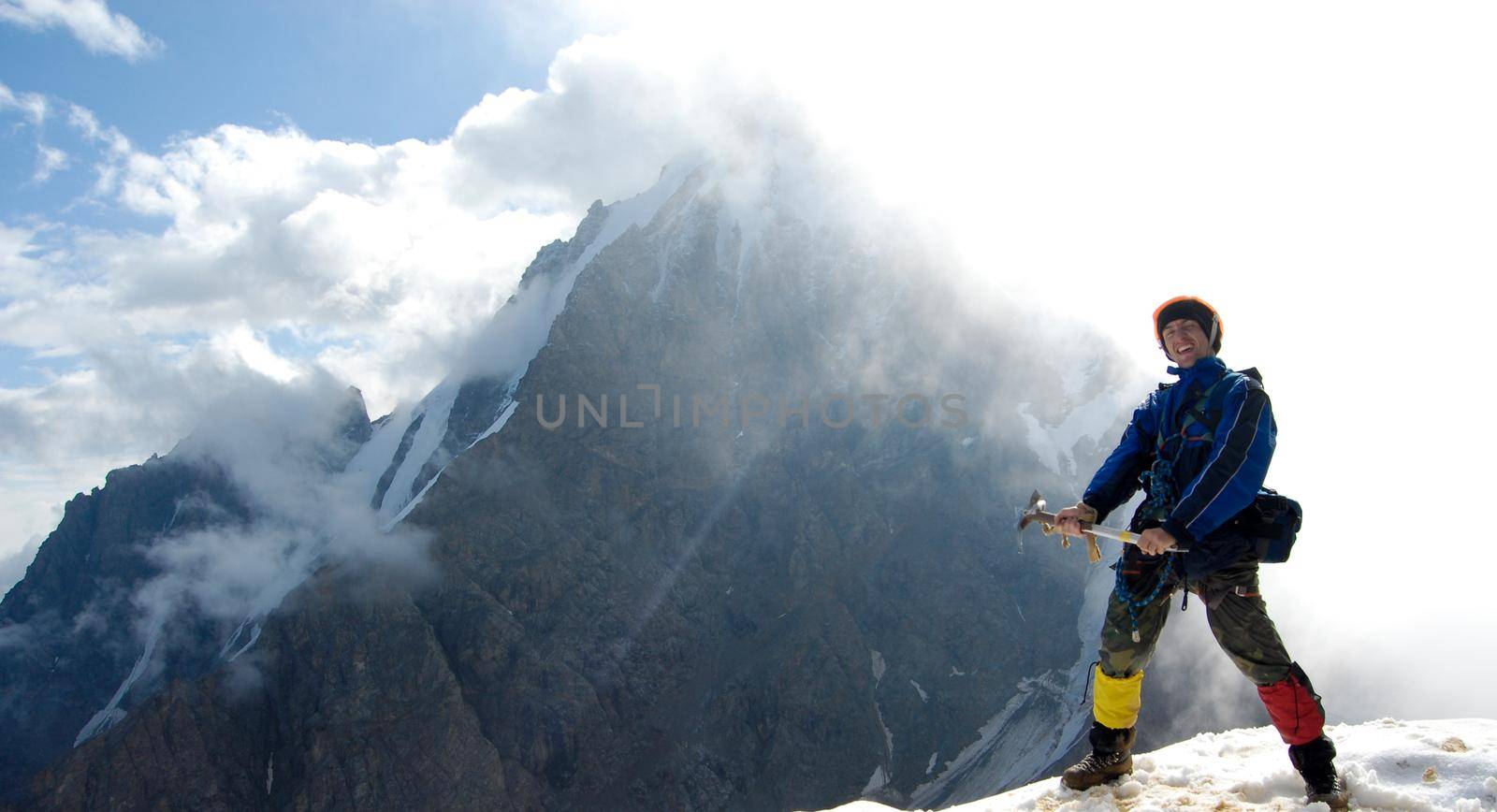 Young mountaineer is standing at the very edge of a rocky mountain top. Behind him is the sun shining right throung the cloud creating great lighting effect