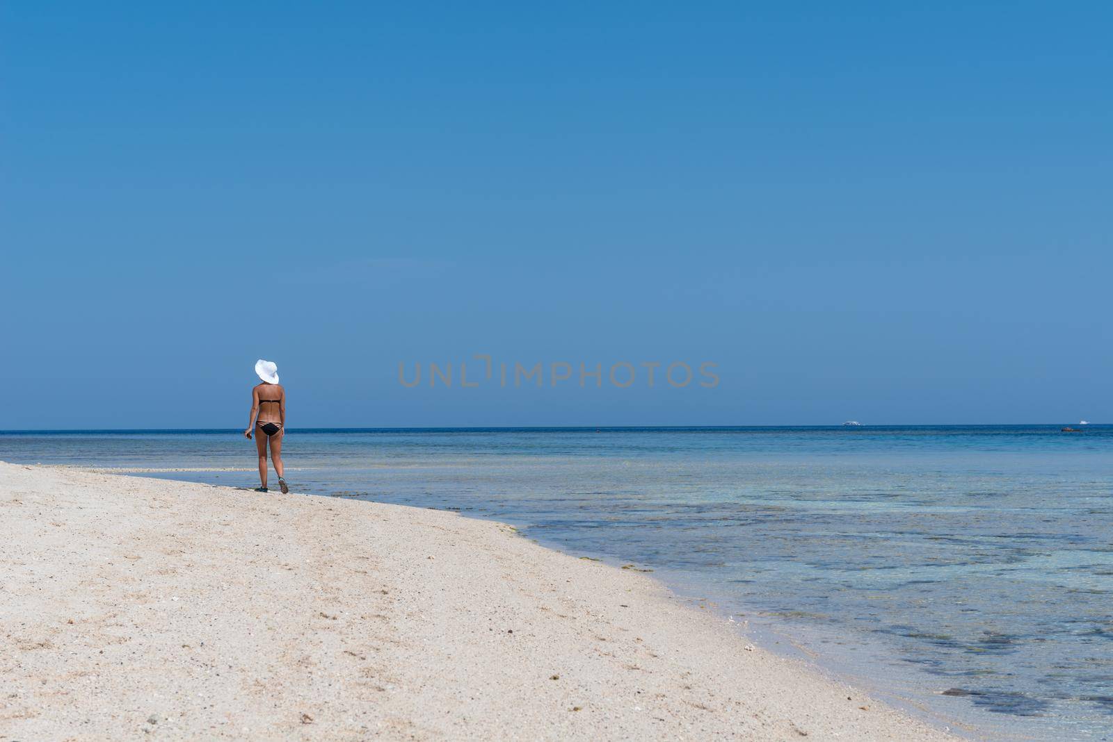 Slim woman wearing white hat walking along beautiful beach