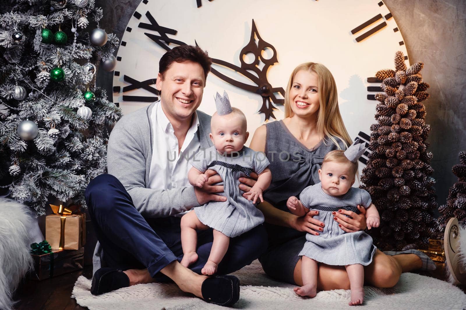 A happy big family with twin children in the New Year's interior of the house against the background of a large clock.