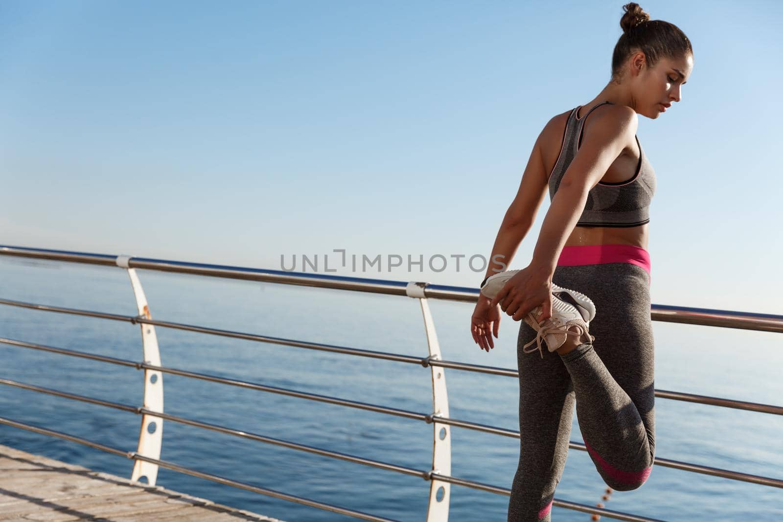 Rear view of sportswoman stretching her leg before running along seaside by Benzoix