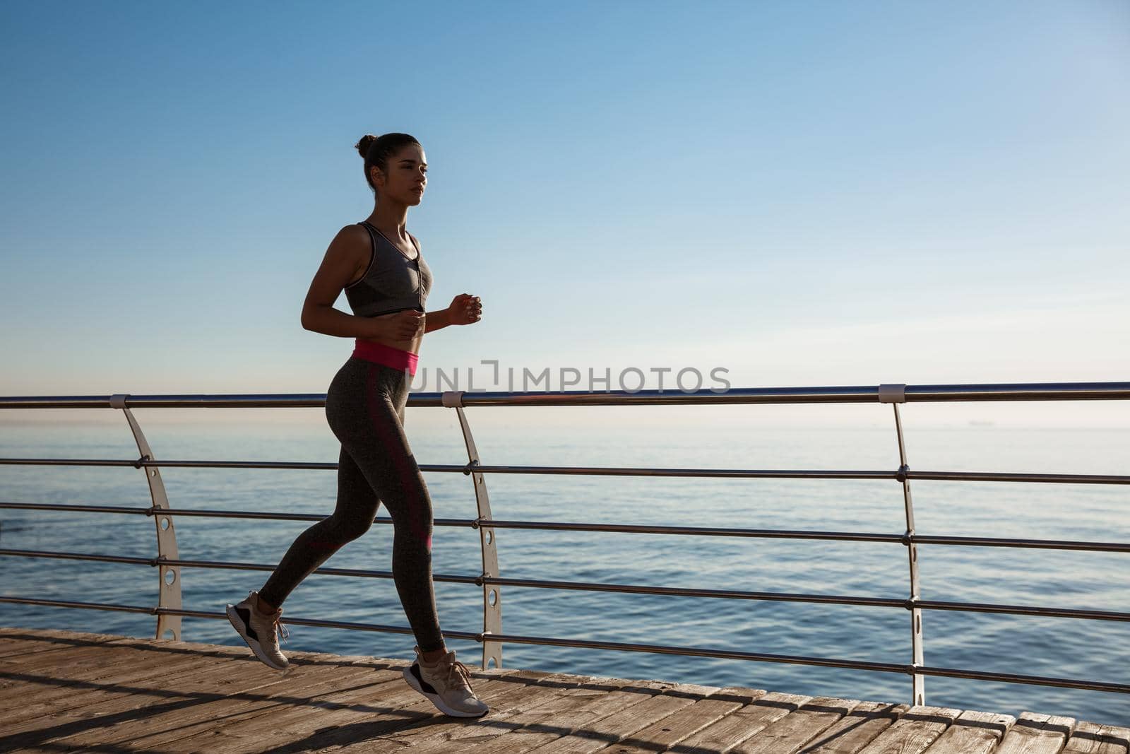 Side view of fitness woman running along seaside promenade, workout on fresh air near the sea.