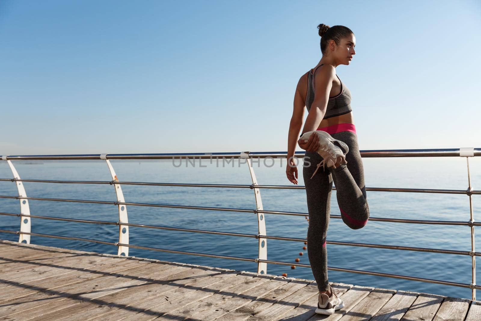 Rear view of sportswoman stretching her leg before running along seaside.