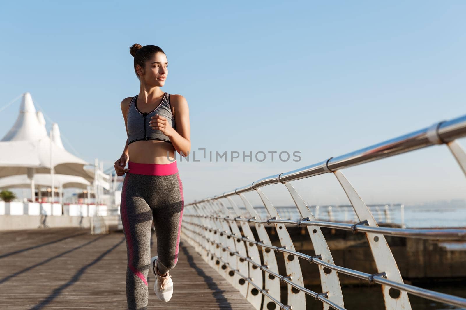 Image of fit and healthy woman jogging in the morning, looking at sea during workout. Female runner training on the seaside promenade.
