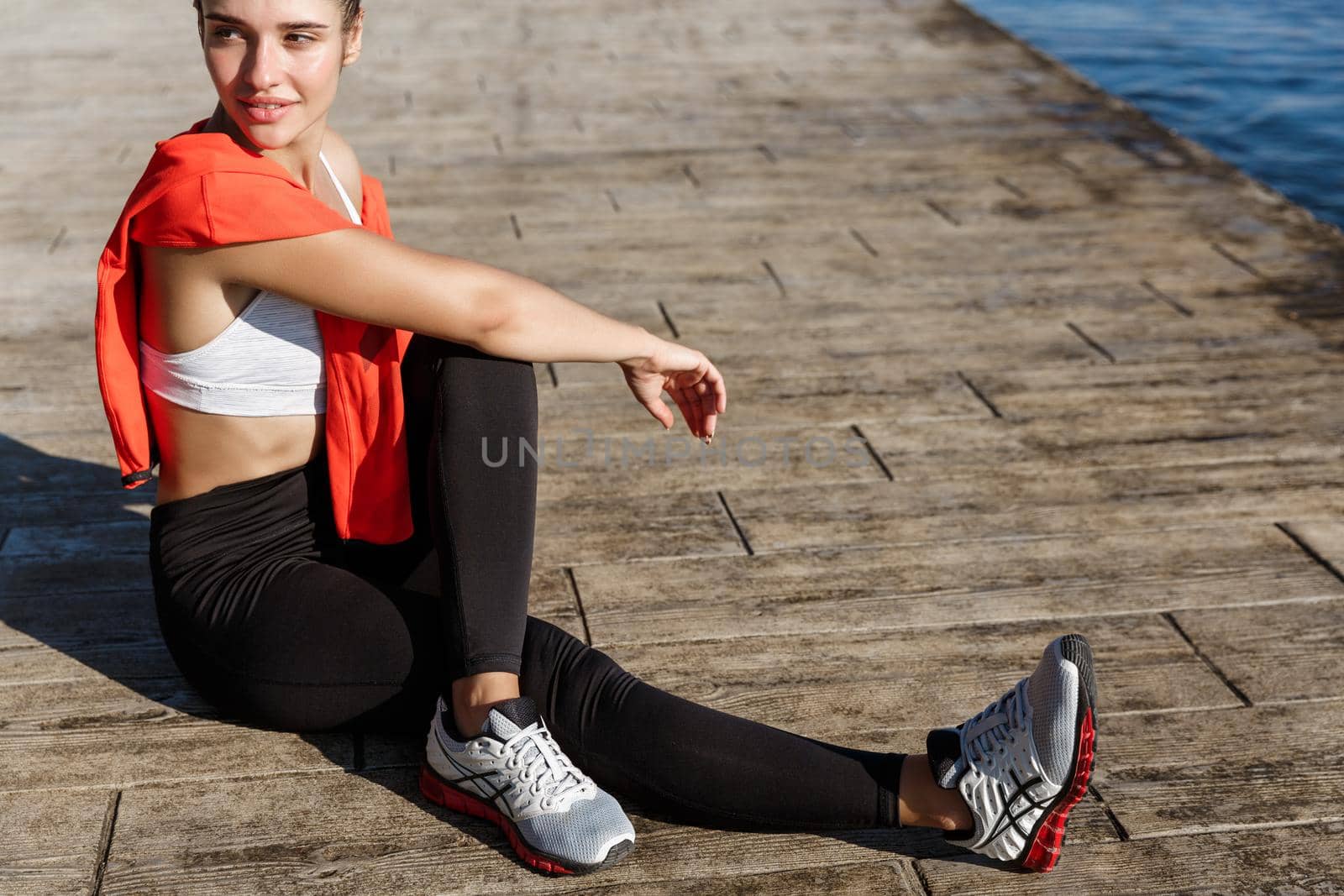 Cropped shot of attractive sportswoman having rest after workout, enjoying view on the sea and smiling by Benzoix