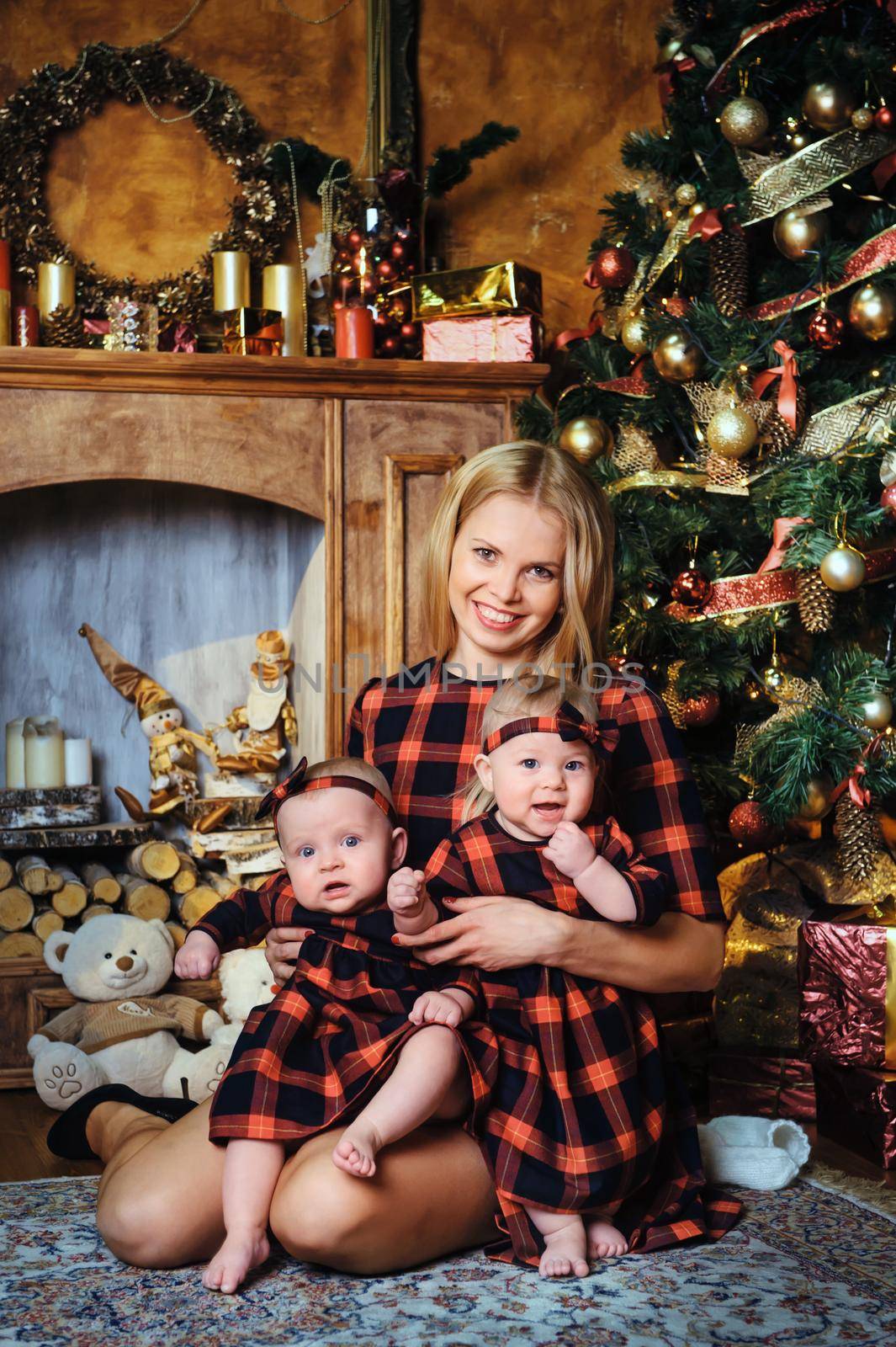 A happy mother with her twin children in the New Year's interior of the house on the background of a Christmas tree by Lobachad