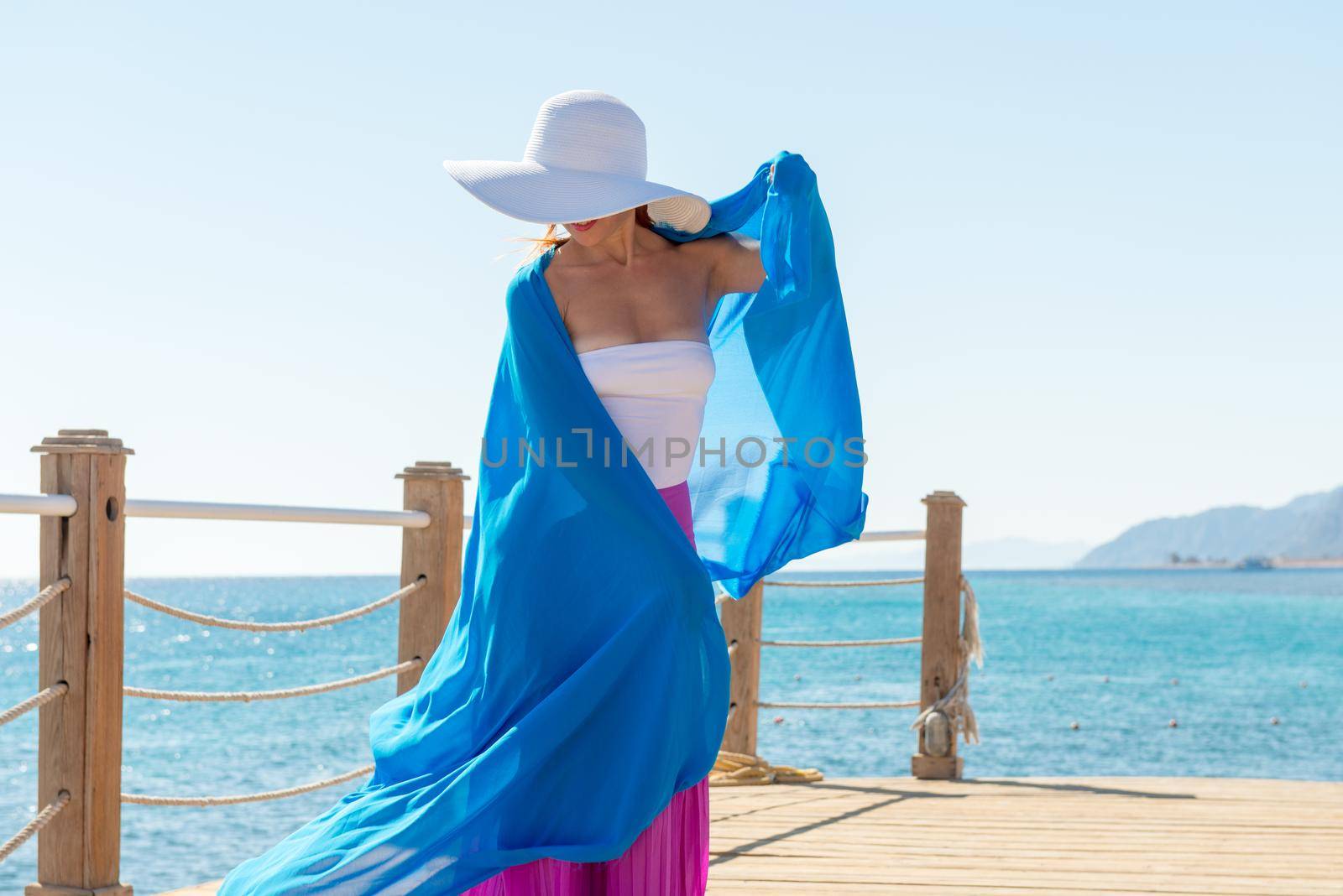 Photo of beautiful young woman wearing hat and blue veil at sea resort