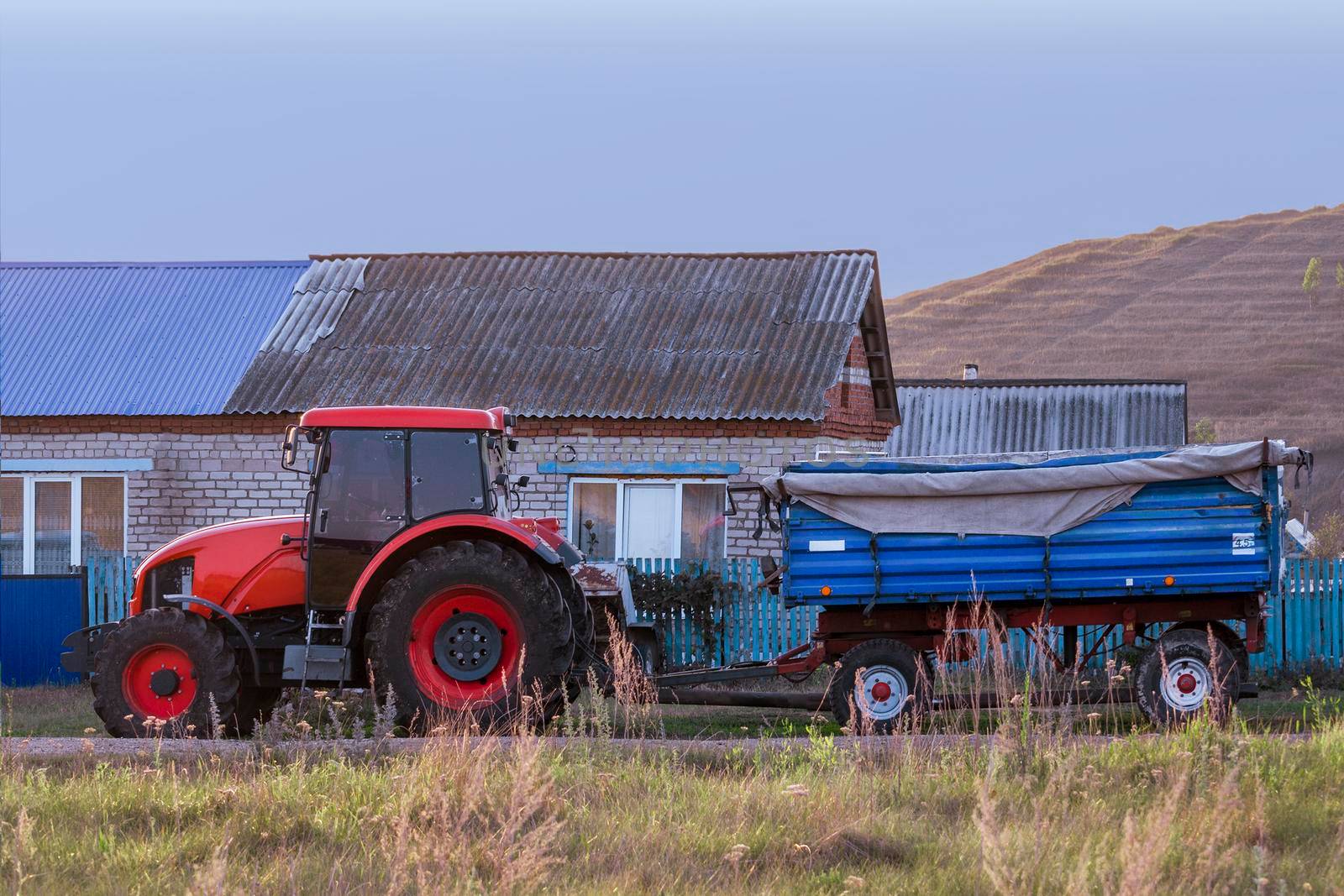 Red new wheeled tractor of medium size with blue trailer. by Essffes