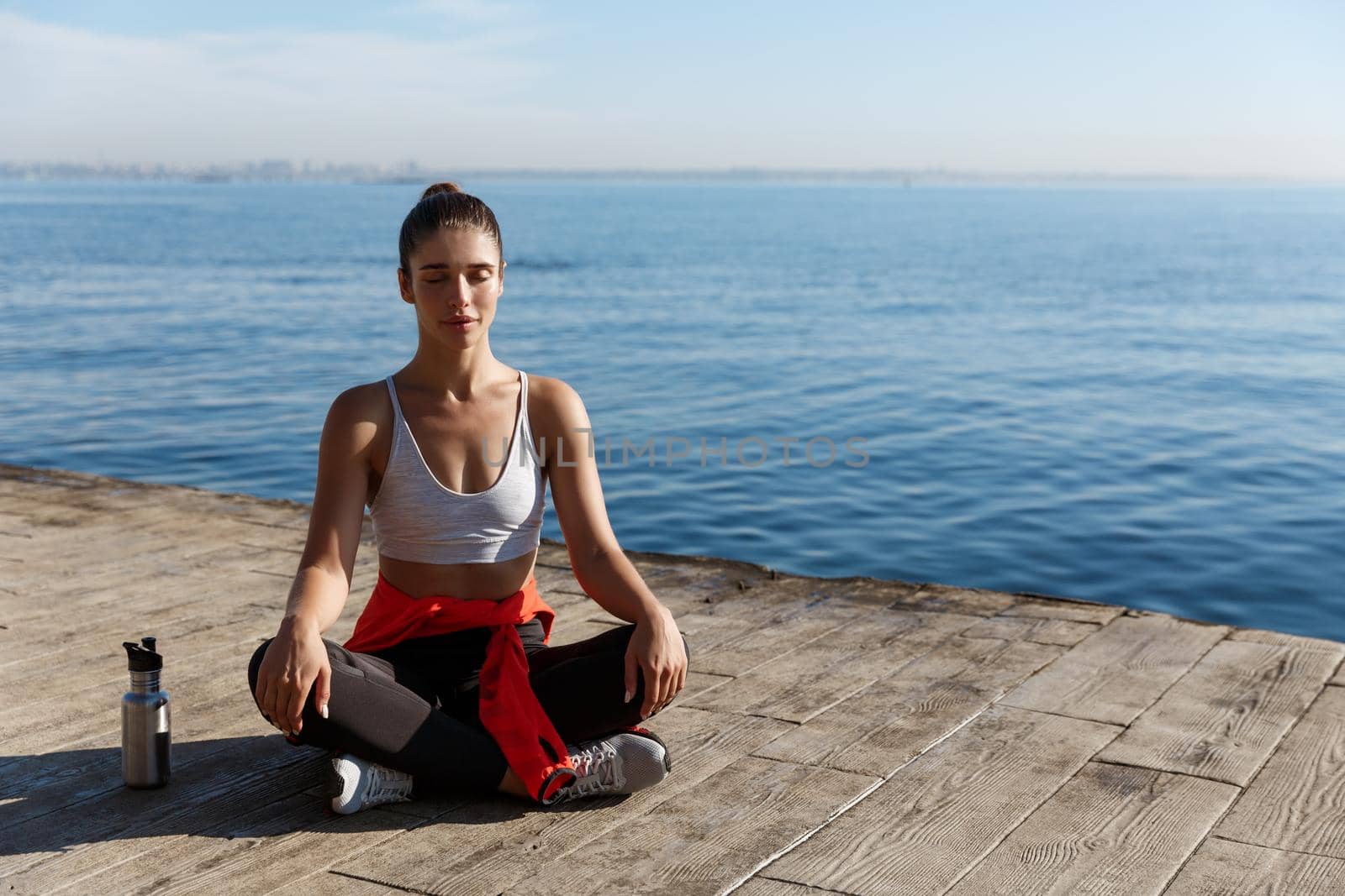 High angle shot of beautiful relaxed woman having yoga training near the sea, meditating on a pier.