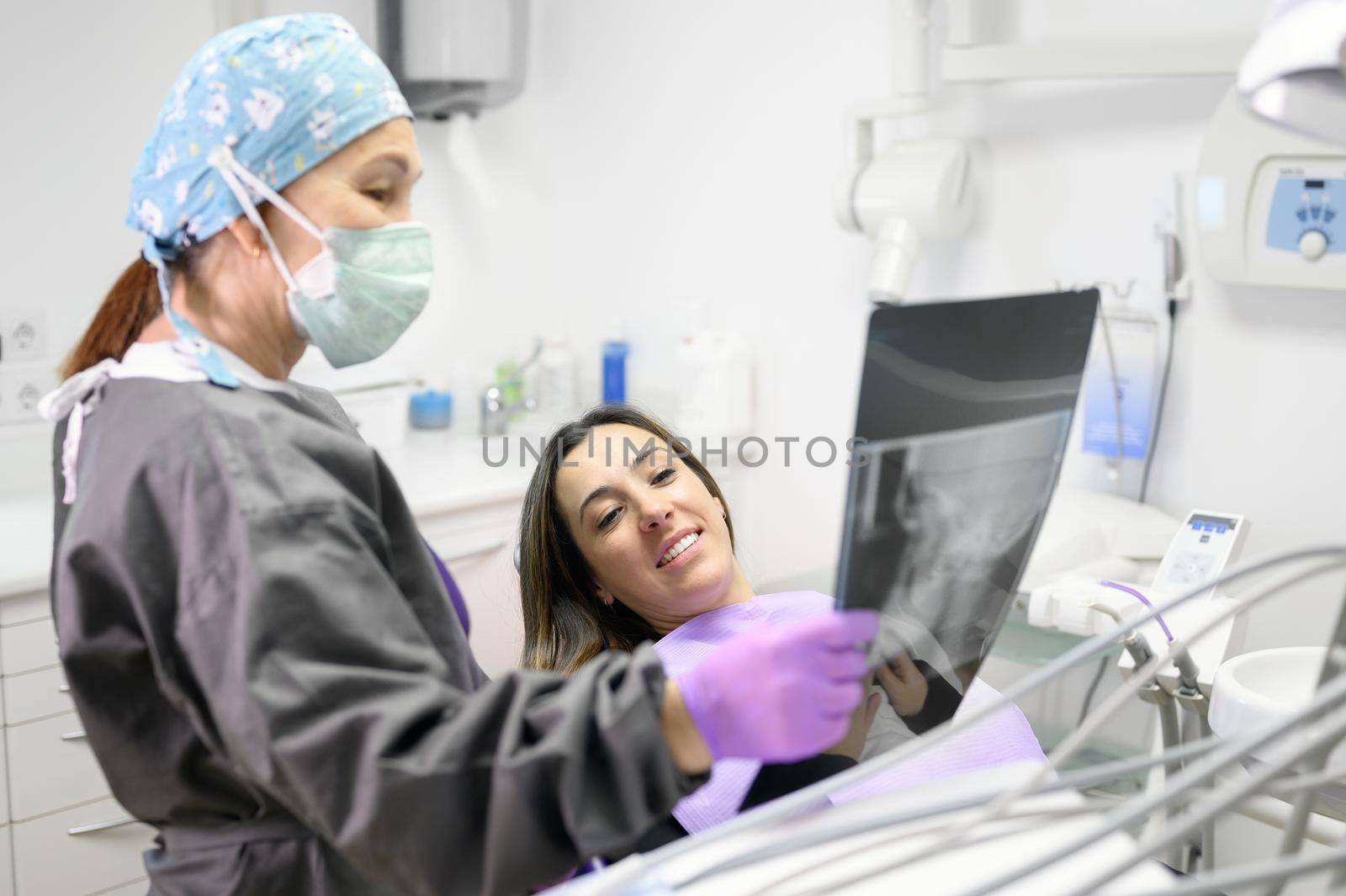 Female dentist pointing at patient's X-ray image in dental office. by HERRAEZ