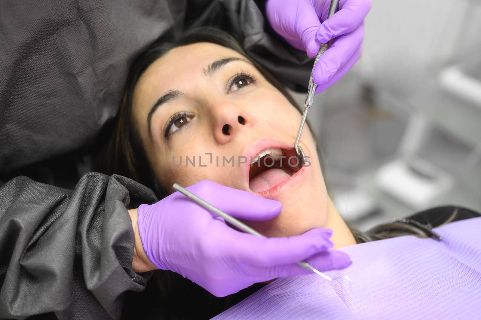 Young woman visit dentistry clinic for professional teeth treatment. Woman dentist bend over patient. Doctor holding instrument tool for oral examination. by HERRAEZ
