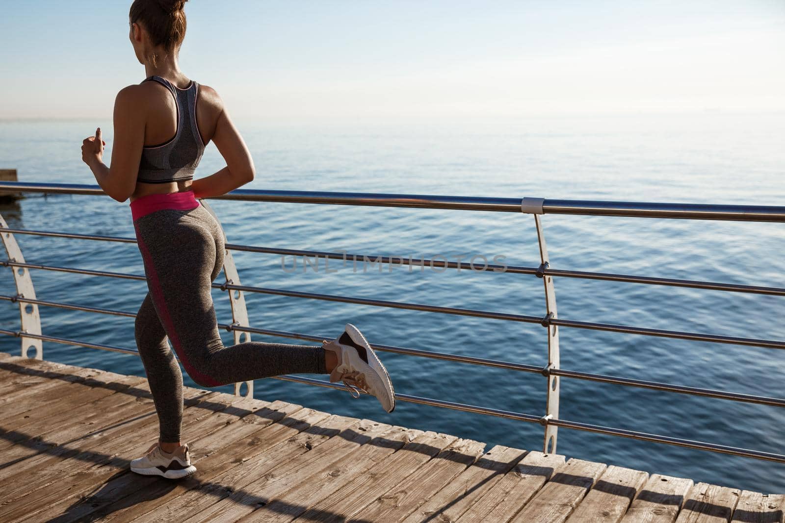 Rear view of young healthy woman workout near the sea. Girl jogging alone, training on seaside promenade.