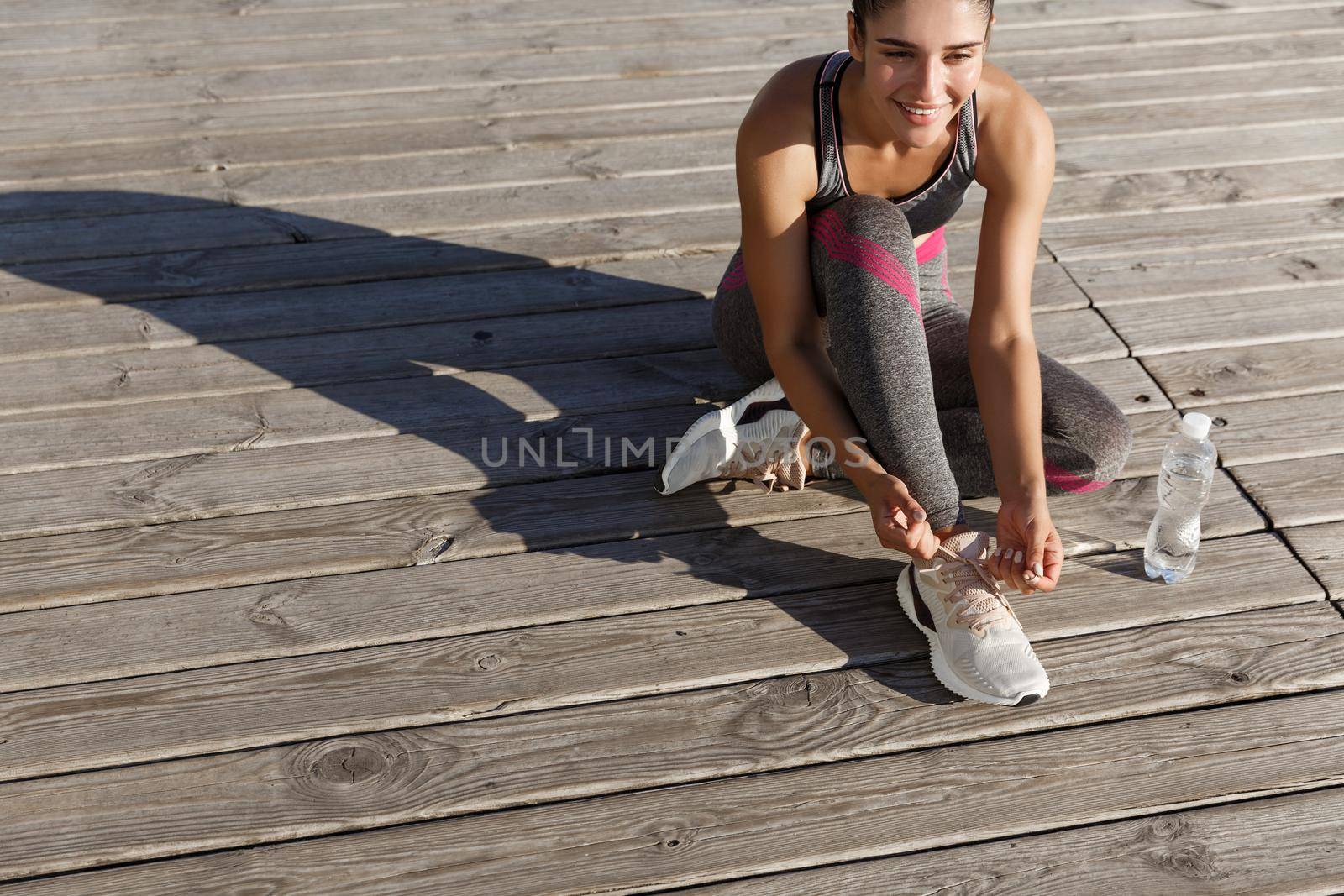 Outdoor shot of young fitness woman tying shoelaces and drinking water during workout by Benzoix