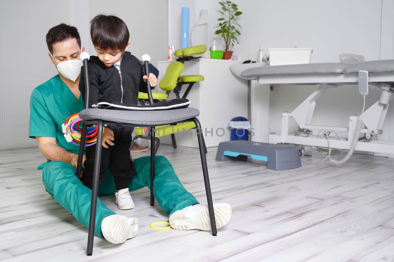 Child with cerebral palsy on physiotherapy in a children therapy center. Boy with disability doing exercises with physiotherapists in rehabitation centre. High quality photo.