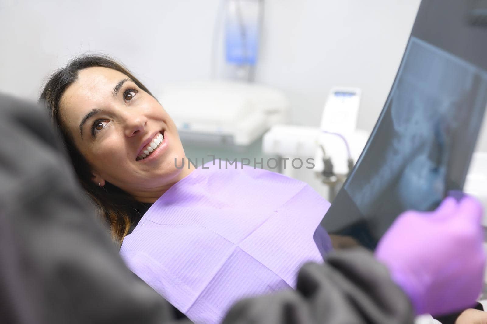 Happy young woman, during the consultation with dentist showing x-ray in the dental office. by HERRAEZ