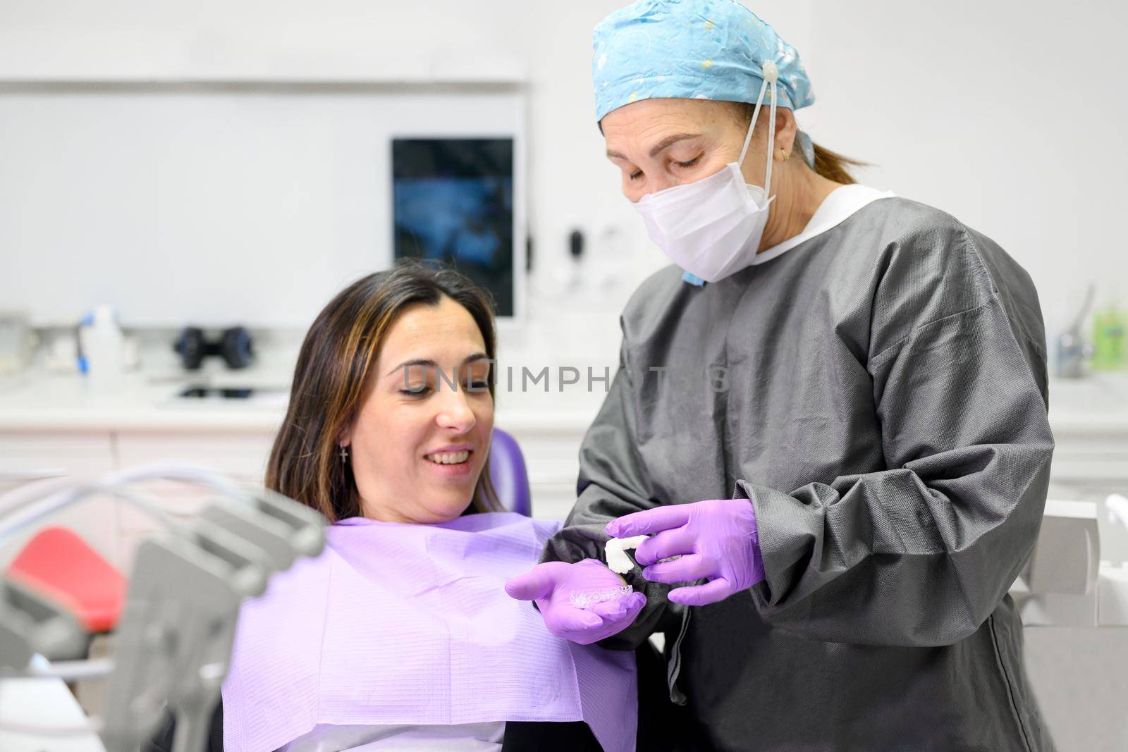 Dentist showing to woman patient an orthodontic silicone trainer. Mobile orthodontic appliance for dental correction. by HERRAEZ