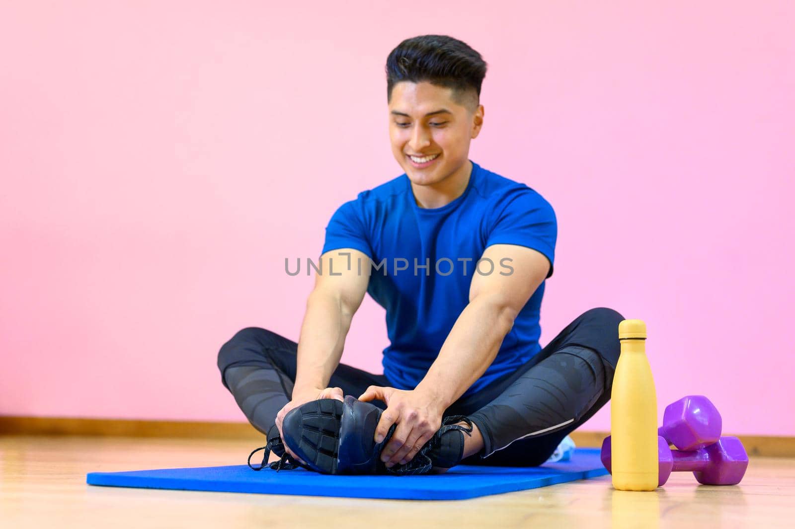 Young Hispanic man practicing yoga on his mat at gym on pink background. by HERRAEZ