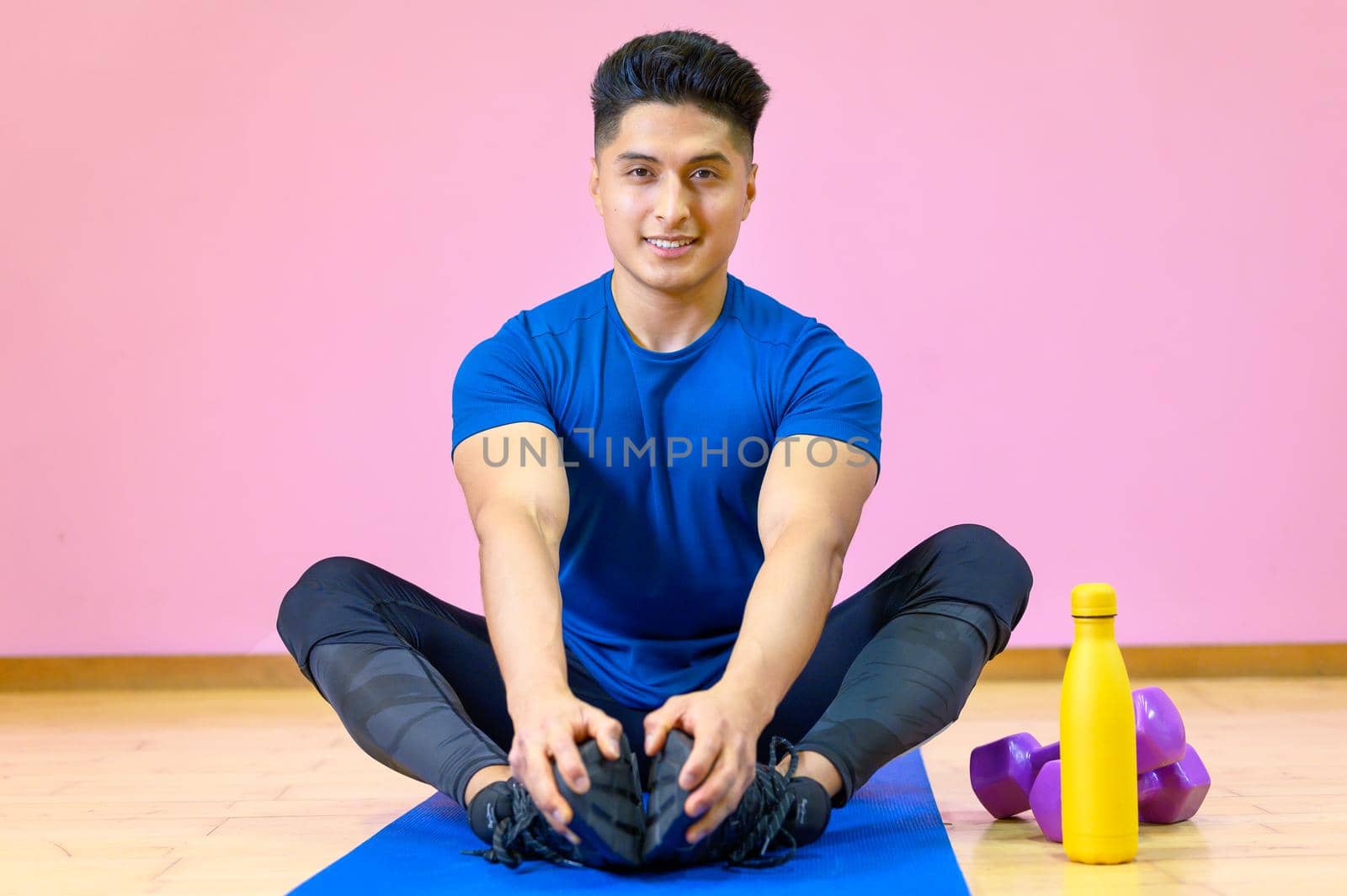 Young Hispanic man practicing yoga on his mat at gym on pink background. by HERRAEZ