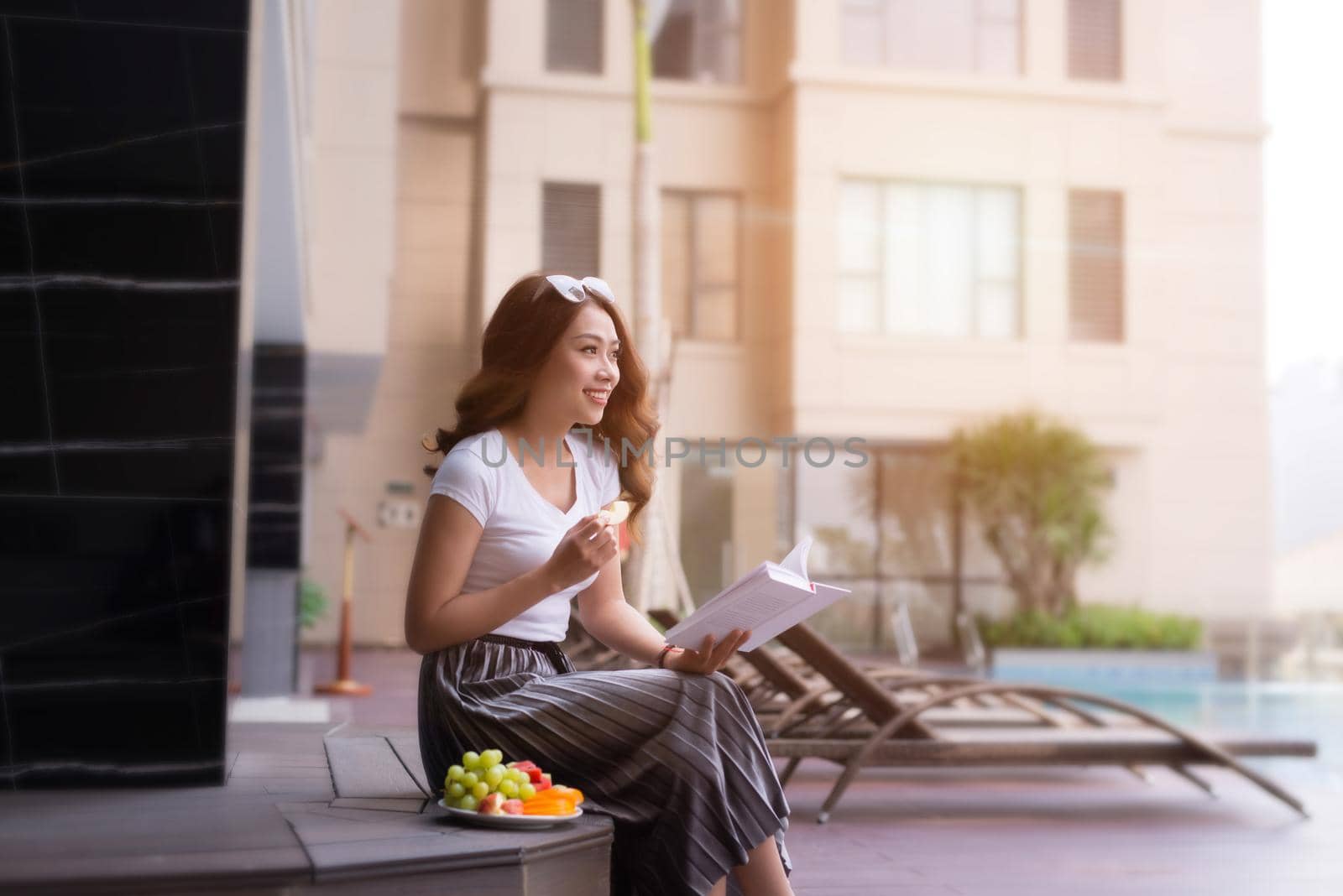 Woman in summer hat reading a book by the swimming pool. Vacation and relaxation, summer travel concept. by makidotvn