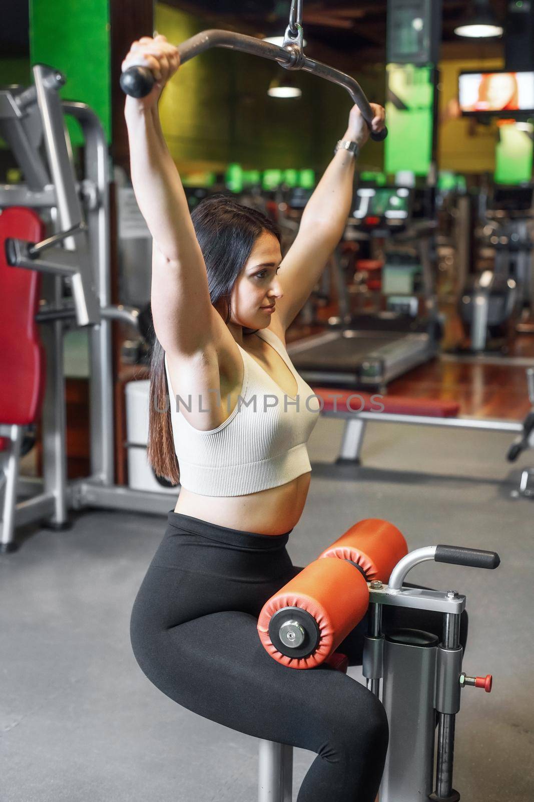 Young sportswoman exercising on lat machine in gym. by HERRAEZ