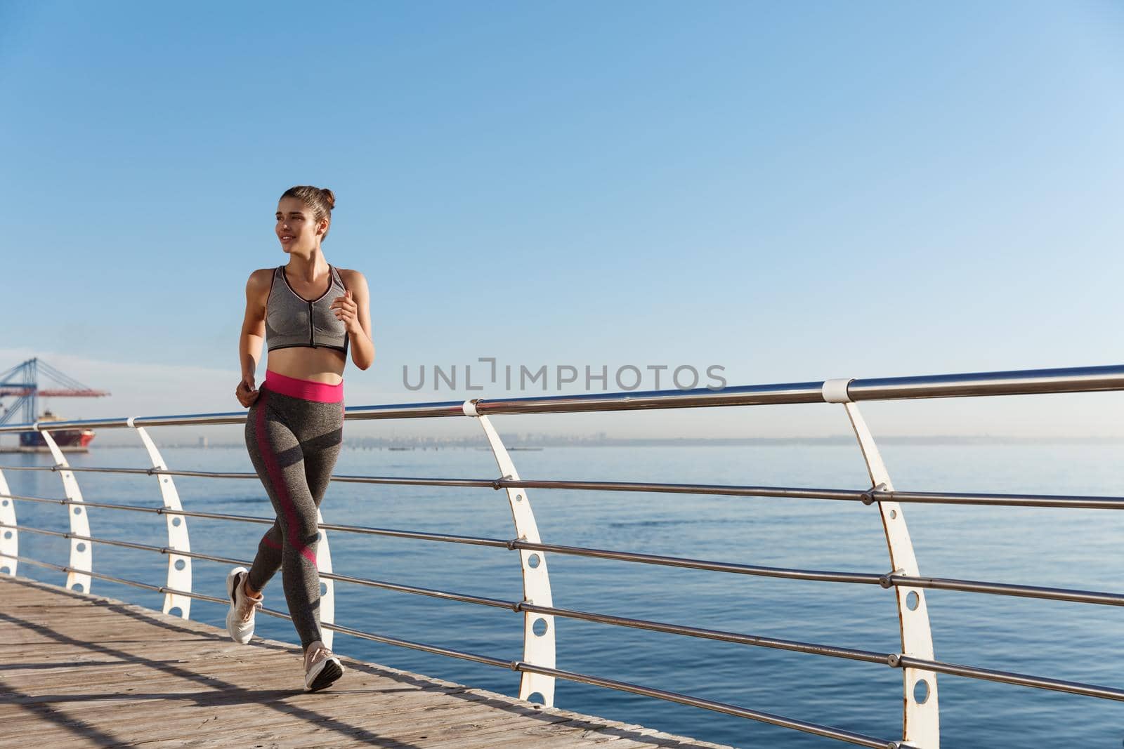 Portrait of healthy attractive fitness woman running near the sea. Girl jogging and smiling outdoors.