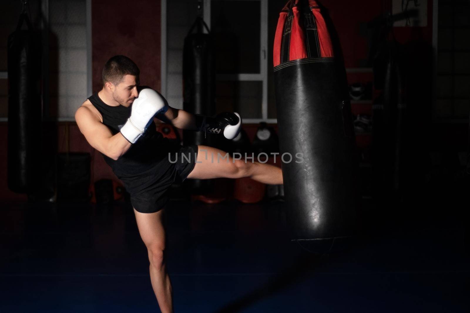 Muscular handsome kickboxing fighter giving a forceful kick during a practise round with a boxing bag. High quality photo