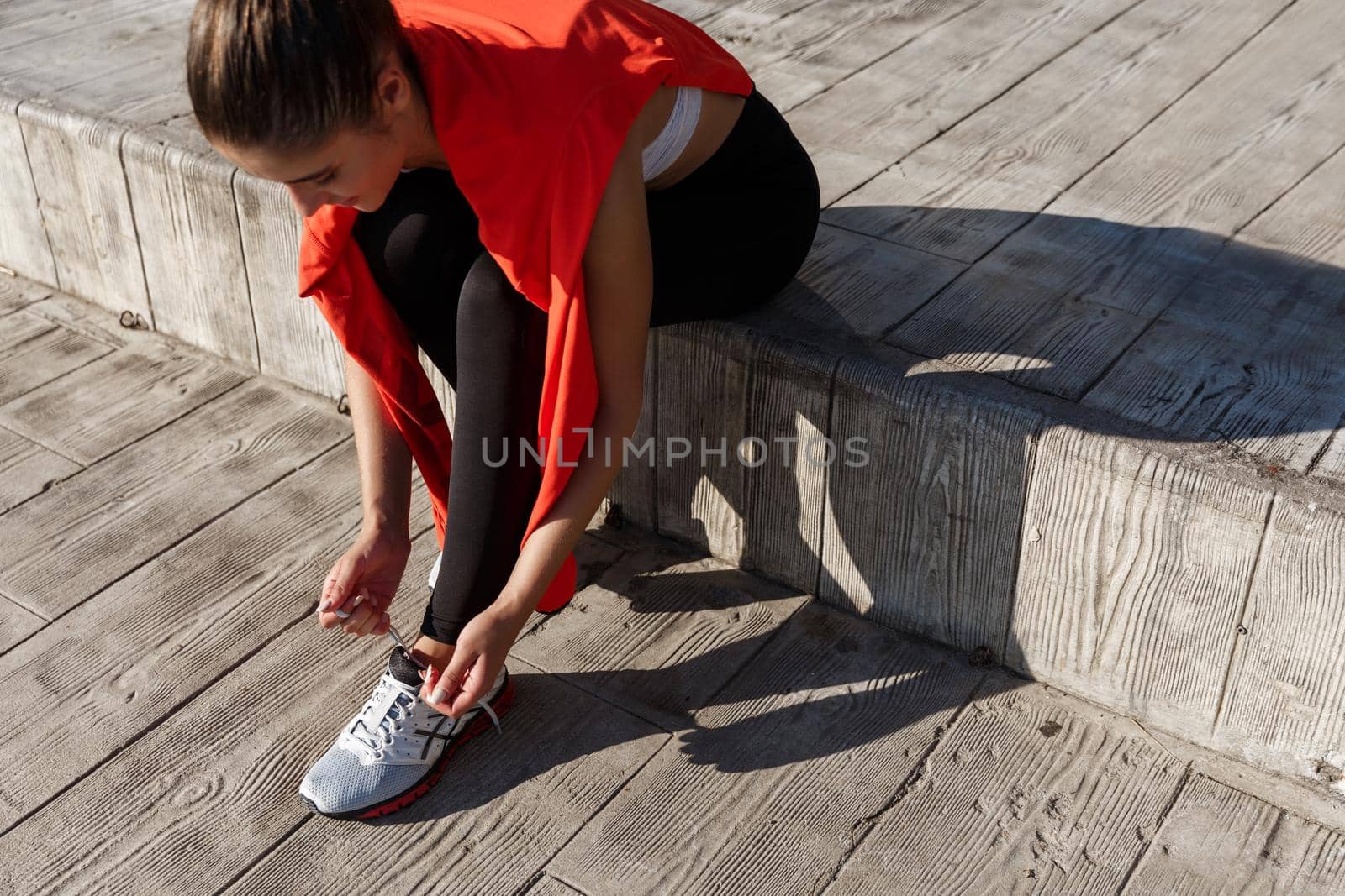 High angle shot of attractive young sportswoman tying her shoelaces before workout or jogging outdoors.