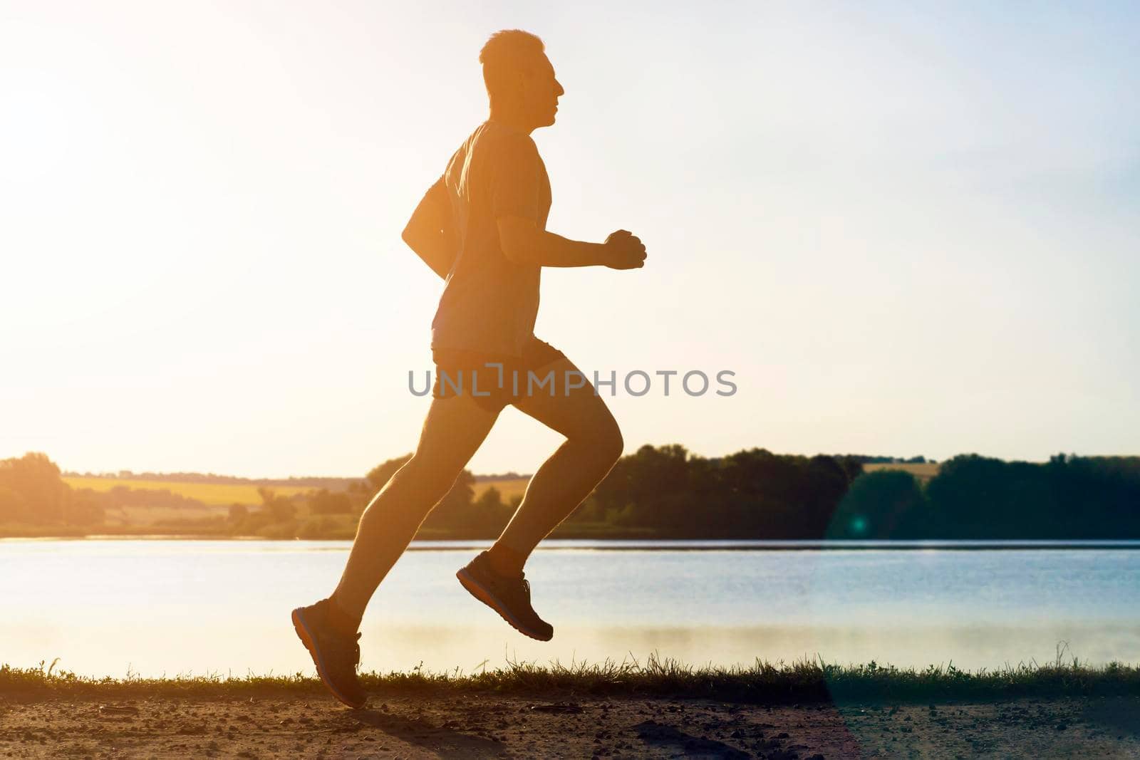 Young man doing cardio workout, exercising and running early in the morning at dawn near a beautiful lake. The athlete is preparing for the marathon.
