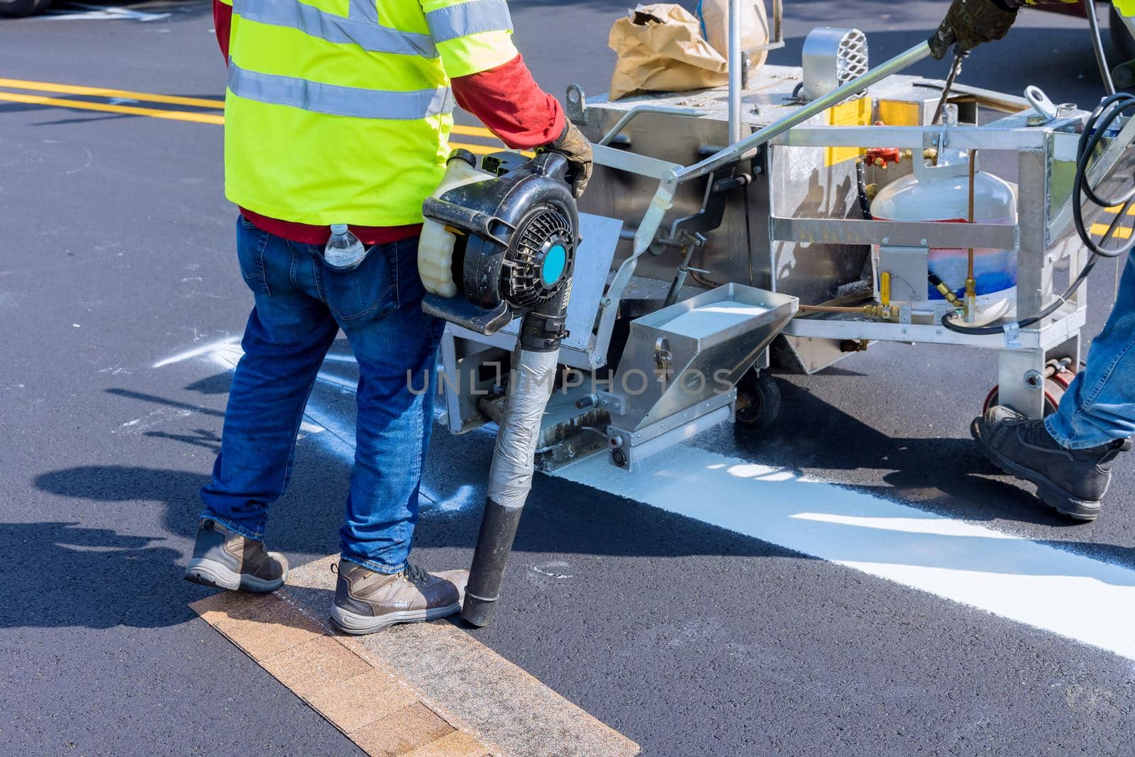 Road construction worker painting white line on the street surface tor thermoplastic spray marking machine during road construction