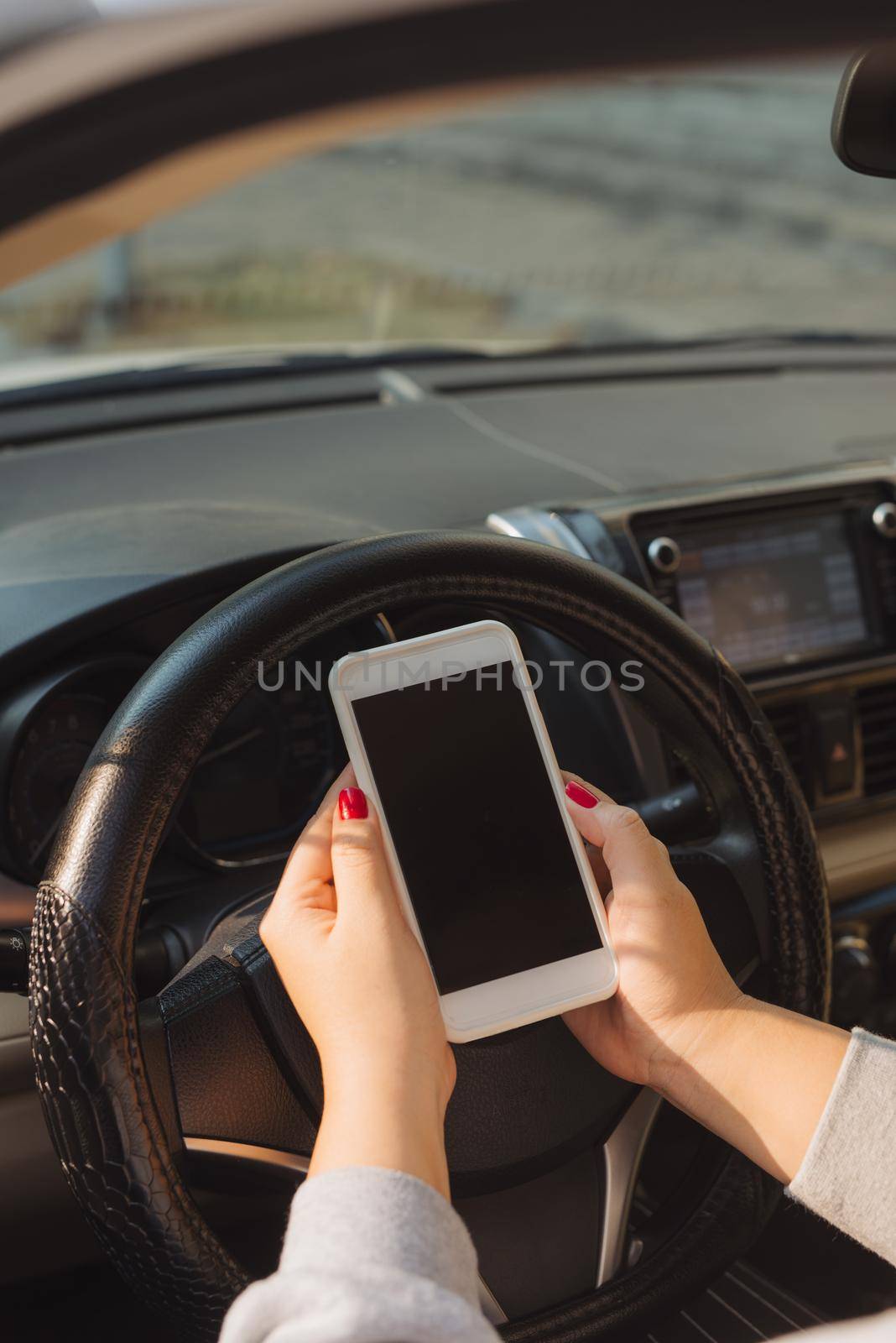 Business woman sitting in car and using her smartphone. Mockup image with female driver and phone screen