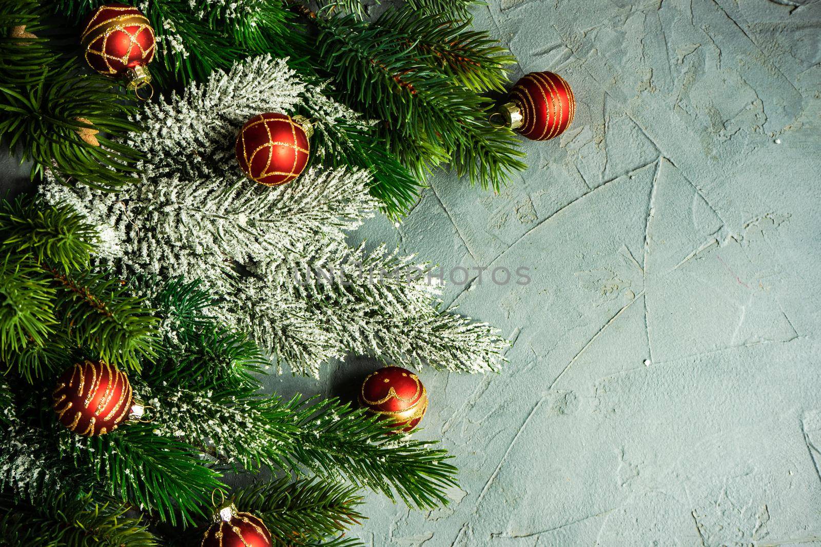 Christmas card concept with frame made with green fir branches, red decoration balls and berries on concrete background